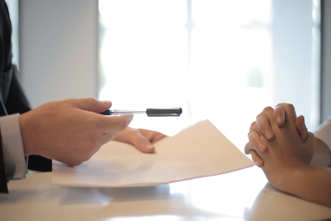 person holding pen and paper and other person with hands crossed on desk