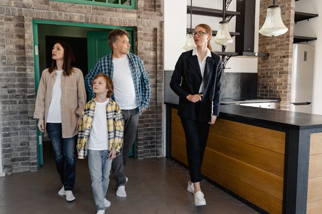 a woman in a suit and glasses leading a family of three through a home